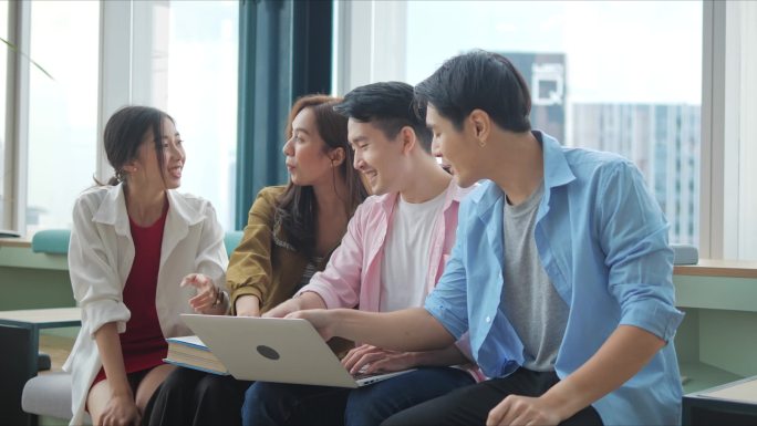一群亚洲高中生聚集在一个办公室的会议室里，用笔记本电脑查看统计数字，分析市场情况，并考虑开展营销活动