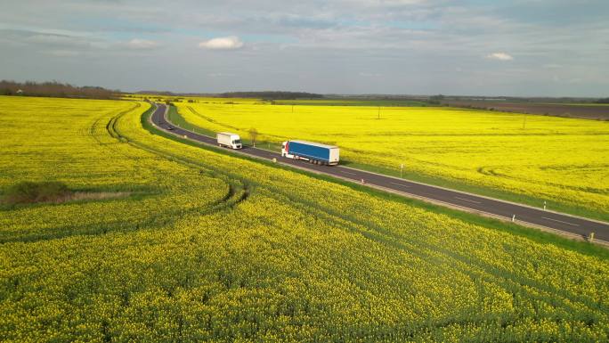 售后服务：货车和汽车在经过黄土的高速公路上行驶。美丽的乡村沥青路面上，环绕着盛开的甘蓝菜农田，交通繁