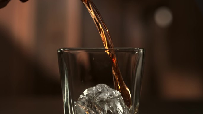 酒，烈酒，晚上好威士忌被倒入一个装有冰块的杯子，慢动作，宏观摄影，木制桌子和黑暗的背景。倒威士忌或朗