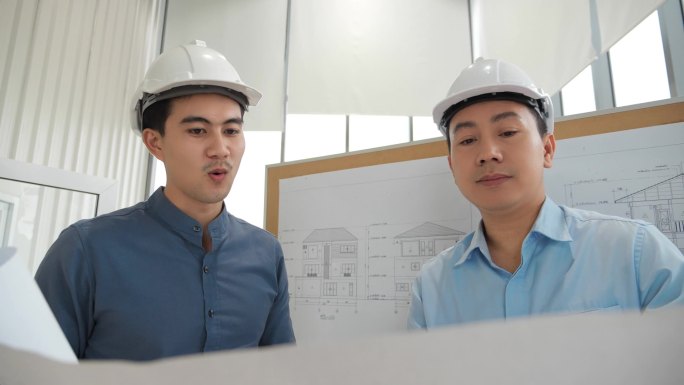 两名亚洲建筑师在办公室设计蓝图，负责讨论业务计划