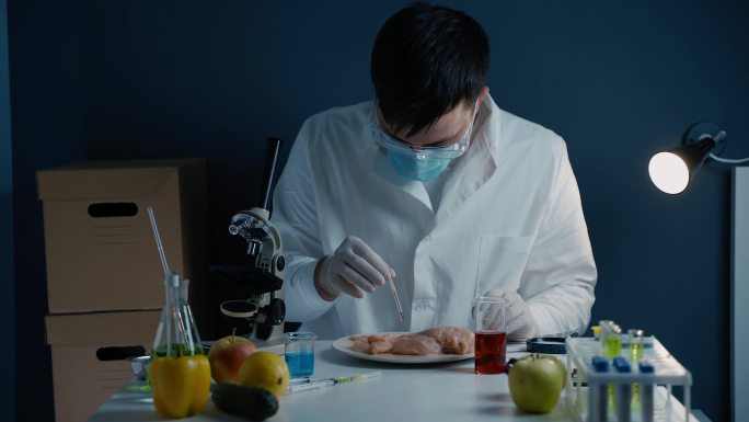 遗传学实验室技术人员从带有移液管的玻璃小瓶中获取红色液体，并将其应用于鸡柳。转基因检测实验室。转基因
