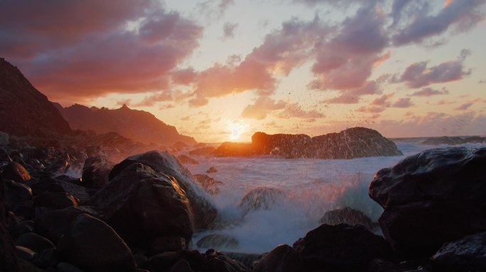 特内里费。橙色的落日落在海面上的岩石海岸上。艳阳高照，夕阳西下，乌云密布。没人