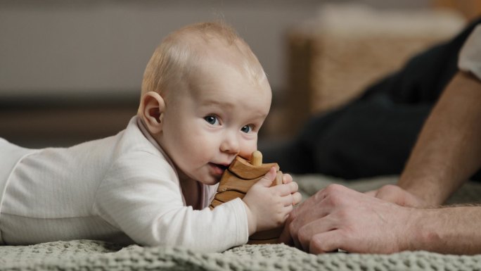 白种人家庭难以辨认的父亲爸爸和小女儿儿子新生儿幼儿躺在地板上玩玩具宝宝咬木结构的概念，男人抚摸着脑袋