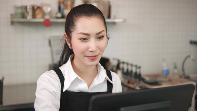 在咖啡店工作的亚洲妇女咖啡店员工。微笑的女服务员收银员向顾客订购咖啡和烘焙。小企业主和非全日制工作概
