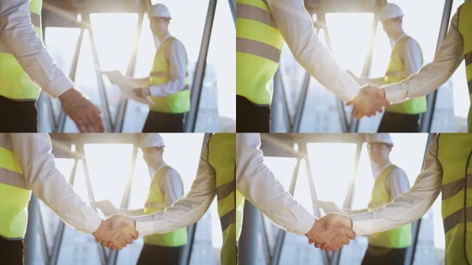 同事与投资者成功交易后与项目计划微笑的模糊工程师握手。专业专家站在高层建筑工地特写