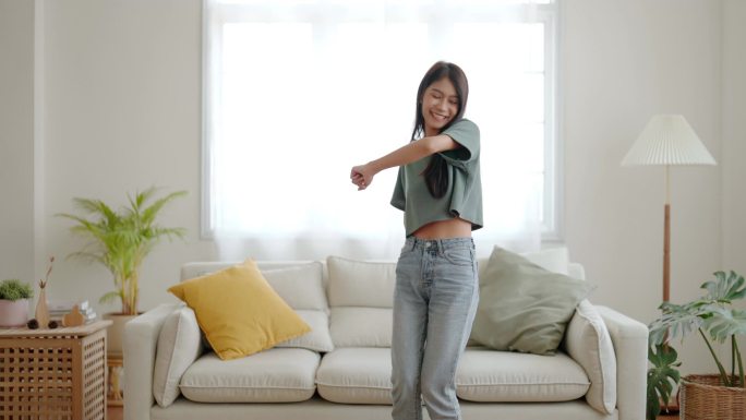 年轻的亚洲女人在家里客厅的地板上跳舞。快乐的亚洲女人笑着在家里放松，健康的精神健康和幸福