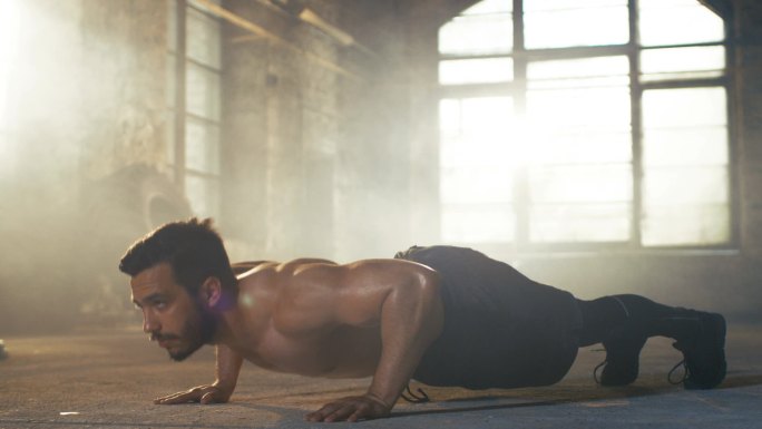 一身是汗的肌肉赤膊男做俯卧撑在健身房改建成一个废弃的工厂。他交叉健身锻炼的一部分 / 高强度间歇训练