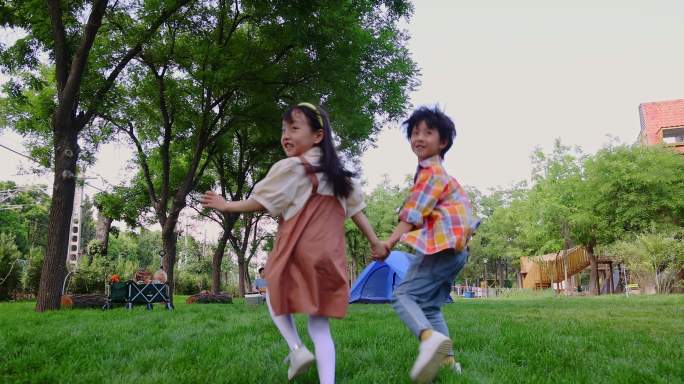两个孩子在草地上手拉手开心奔跑回头看