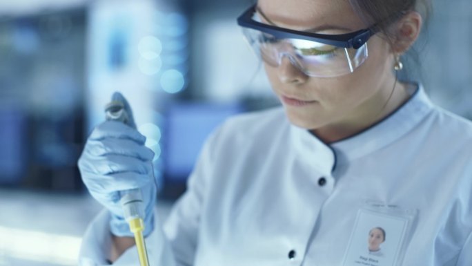 女性研究的科学家在一个大型的现代化实验室使用微管吸吮灌装试管。在背景科学家的工作.