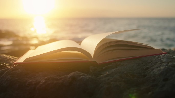 日落时带着光芒在海滩上翻开的书.背景上的海浪。智慧教育科学概念.