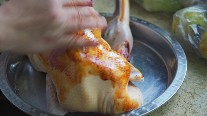 厨房里一位厨师在备菜，腌制一整只鸭子