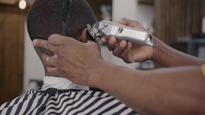 美发师在理发店用剃须机治疗非裔美国顾客的后视图
