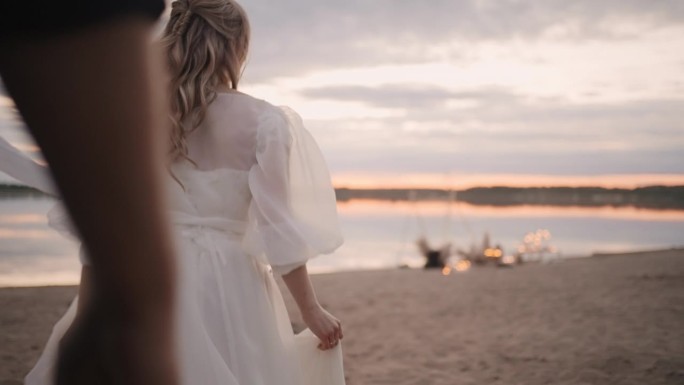 新娘和新郎在日落的海滩上，男人解开女人的腰带，女人在沙滩上奔跑