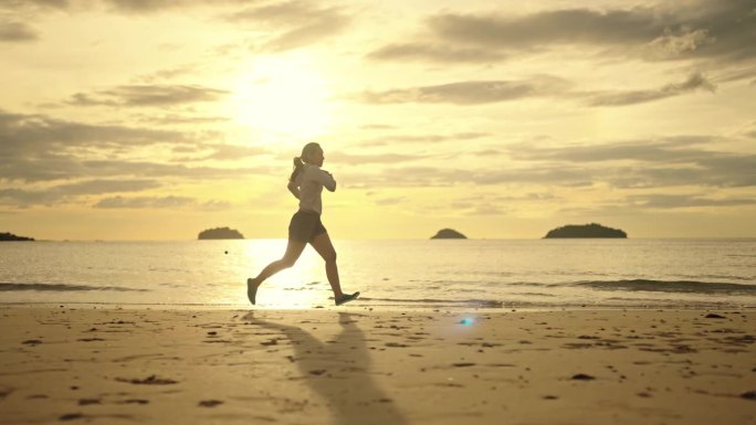 日落时分在沙滩上跑步的亚洲女人