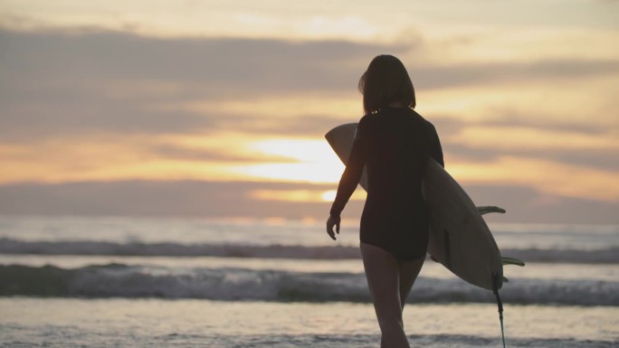 夕阳下的热带海滩上，冲浪女孩手持冲浪板的剪影。