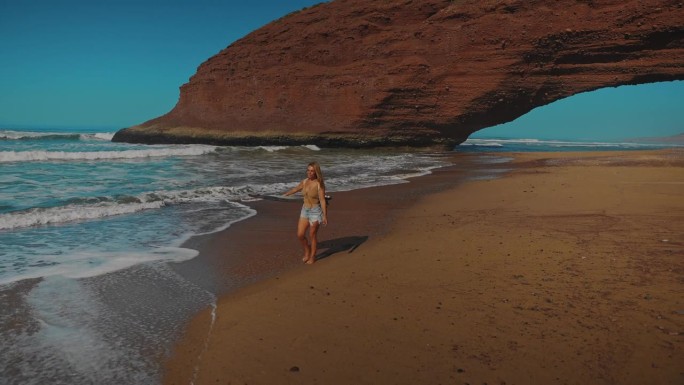宁静的海滩散步，海浪和女人拿着冲浪板，岩石形成的背景