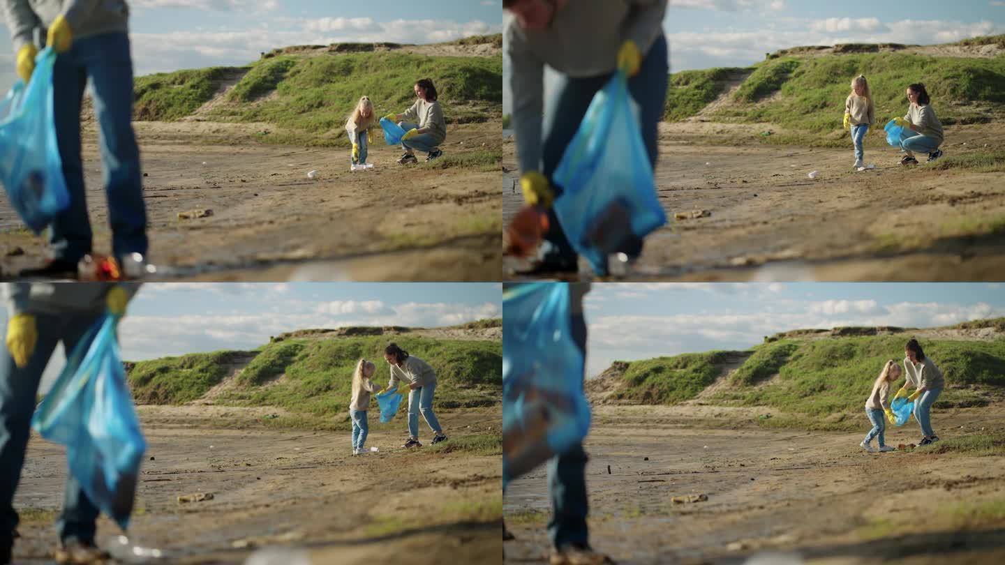 一家人清理河滩上的塑料垃圾，小女孩和她的妈妈把垃圾装进袋子里