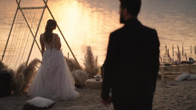 美丽的新娘和迷人的新郎在沙滩上夕阳的剪影，后景，浪漫的婚礼