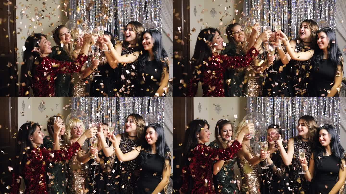 在新年晚会上，年轻迷人的女士们穿着闪闪发光的裙子欢呼着，在飞舞的五彩纸屑中喝着香槟。超级慢动作。