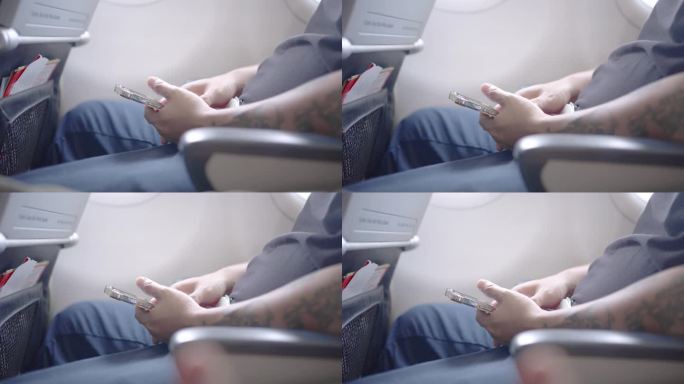 一名男子在飞行途中坐在飞机靠窗的地方玩智能手机。