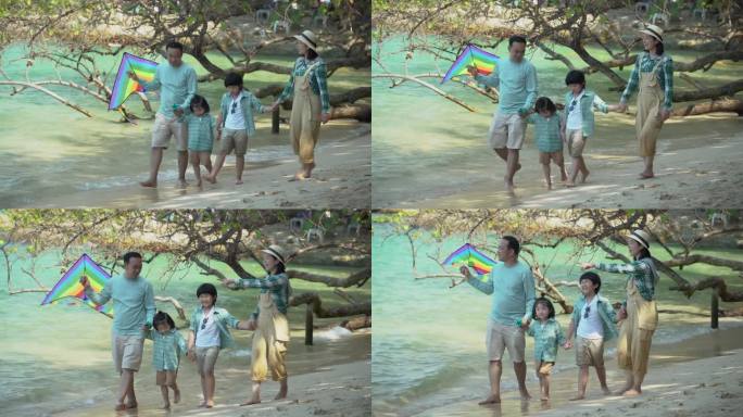 快乐的亚洲家庭散步和手牵风筝在海滩上一起旅行在假期暑假。妈妈爸爸女儿儿子暑假旅行。穿着相似的服装。