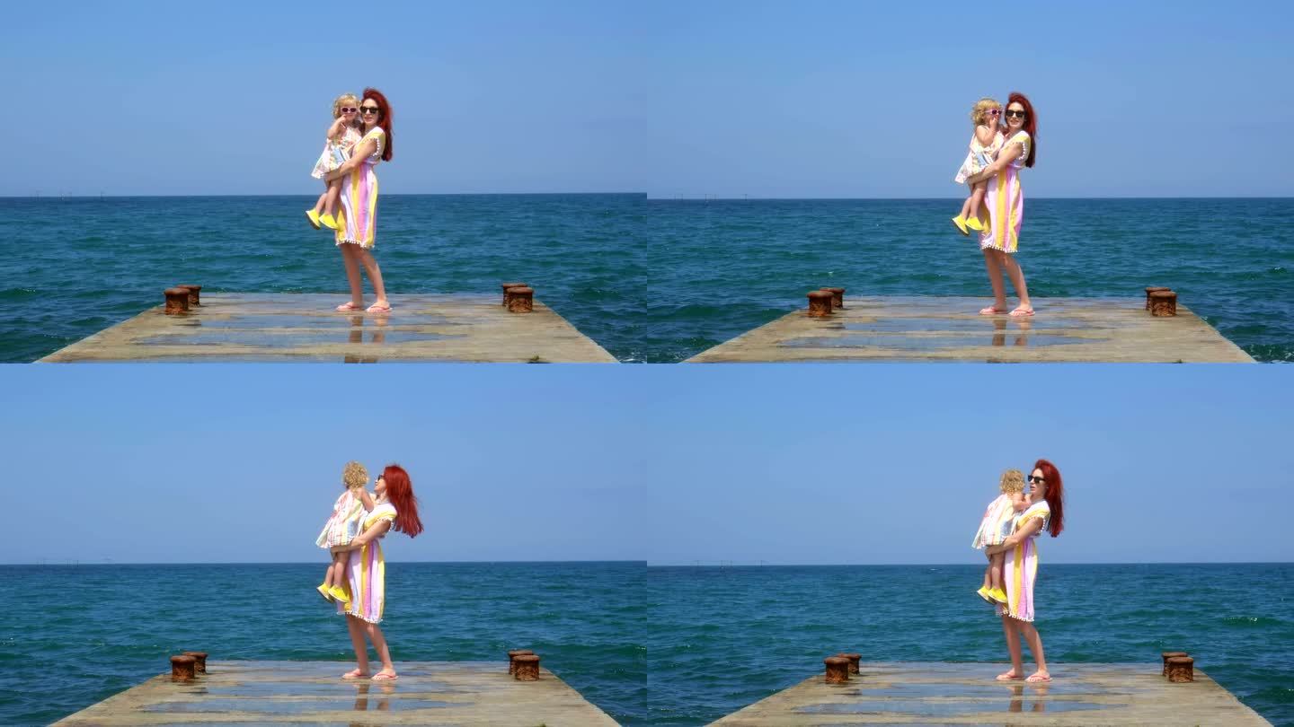 母亲抱着女儿站在海边的码头上