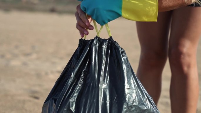 垃圾袋站在海滩上，女人收集垃圾，把它放进袋子里，合上袋子