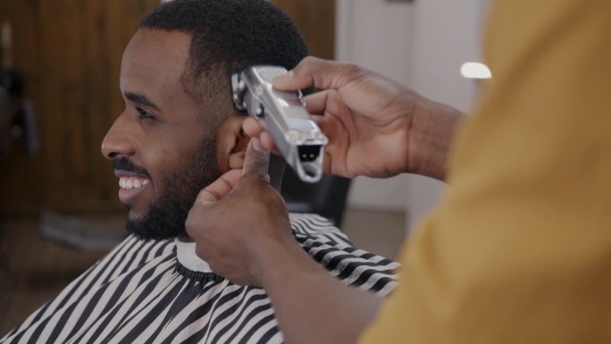 理发师在理发店用剃须机剃毛时，一个非洲裔美国人微笑的侧视图