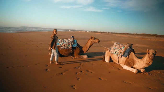 在撒哈拉沙漠的沙滩上，女游客带着骆驼休息