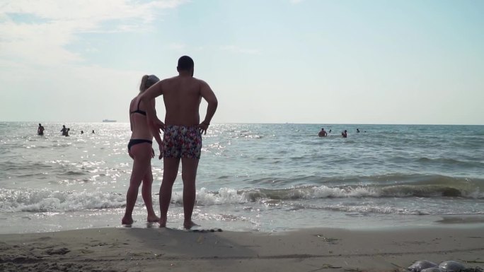 一对幸福的年轻夫妇站在海边享受他们的假期。微笑的情侣度假的概念。慢动作