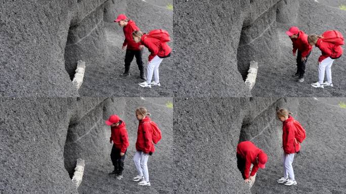 身穿红色夹克、背着双肩包的两名欧洲少年(男、女)正在徒步旅行，他们仔细地环顾四周，进入了一个山洞。青