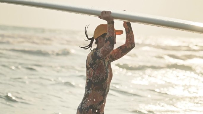 日落时分，女冲浪者在沙滩上拿着冲浪板奔跑，慢动作