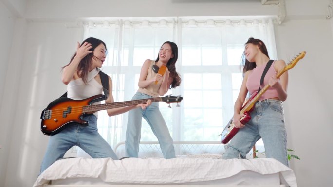 亚洲女人在床上弹电吉他和电贝斯唱歌