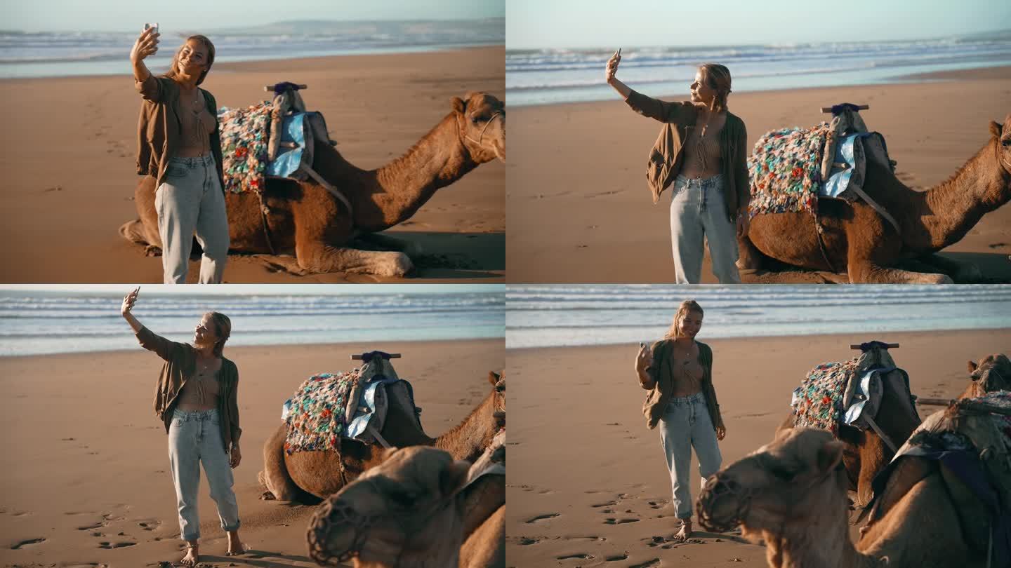 在撒哈拉沙漠的沙滩上，女游客与休息的骆驼自拍