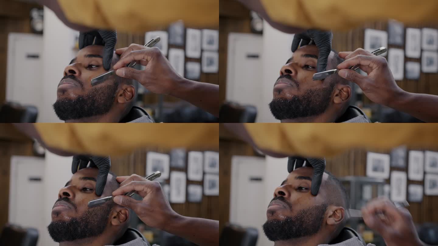 细心的理发师用金属剃刀刮胡子的特写，非洲裔美国人在理发店享受高品质的待遇