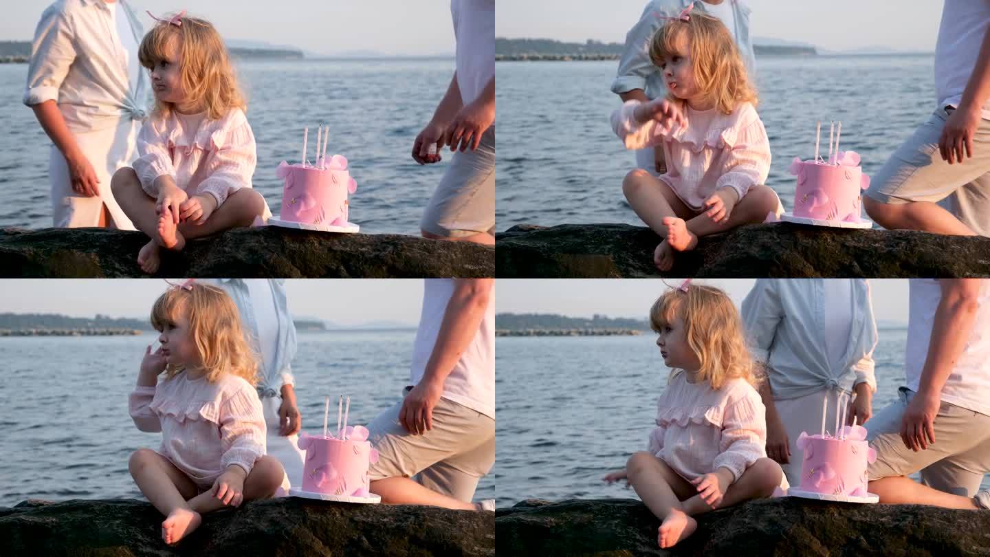 小可爱的金发女孩看着远处用她的手可爱的三支蜡烛蛋糕3年在背景夫妻父母在一起家庭假期生日大海海洋海滩爱