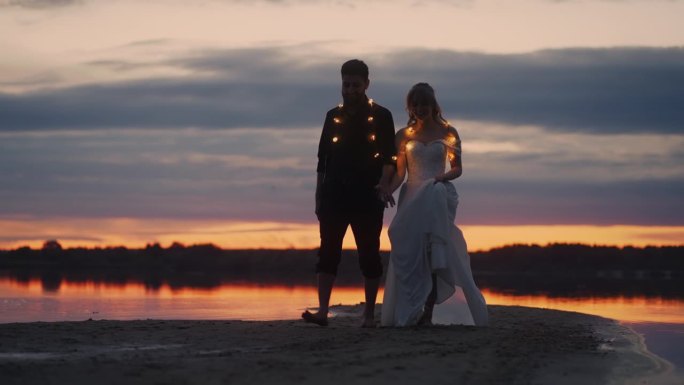 日落后走在沙滩上的新婚夫妇，红色地平线衬托下的新郎和新娘的全身肖像