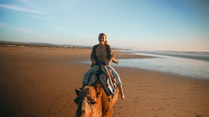 兴致勃勃的女游客沿着海岸线骑骆驼