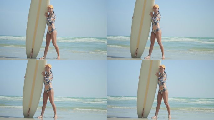 女冲浪者拿着冲浪板，看着镜头，在海滩上微笑