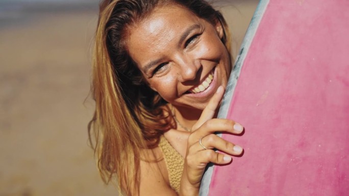 一个女人站在粉蓝相间的冲浪板后面望向镜头