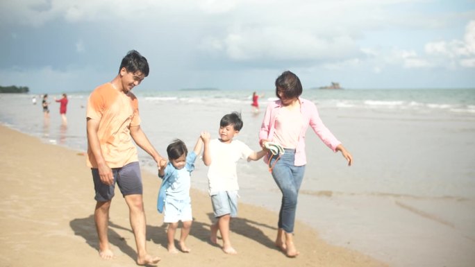 一个亚洲家庭在海滩上散步，心情愉快