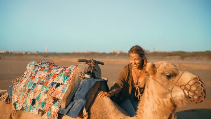 在撒哈拉沙漠的沙滩上，女游客抚摸骆驼，与骆驼玩耍
