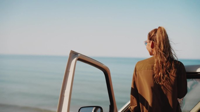 一名女子站在沙滩上的露营车门边，享受着美景和海风