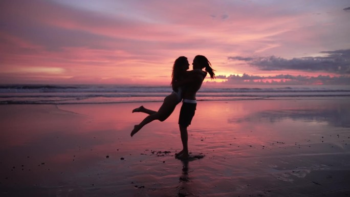 一对相爱的人在海边，日落和海水。现代白人家庭的两个恋人在舞蹈或拥抱中拥抱。健康的漂亮女人和迷人的英俊