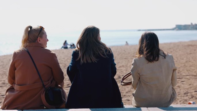 三个女人并排坐在巴塞罗那海滩上。享受户外的阳光