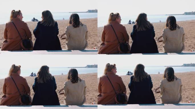 三个女人并排坐在巴塞罗那海滩上。享受户外的阳光