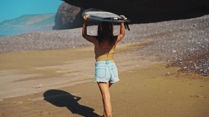 一个女人在沙滩上享受阳光明媚的一天，她把冲浪板举过头顶