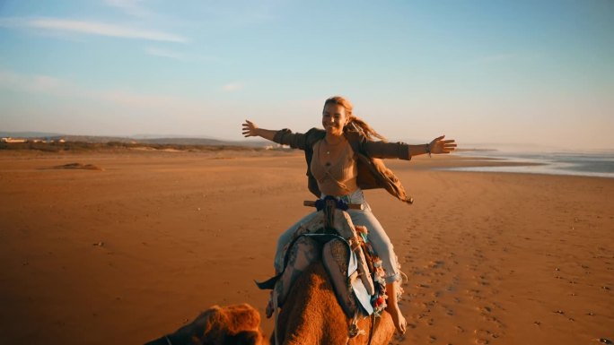 一名女子在沙滩上伸开双臂骑骆驼