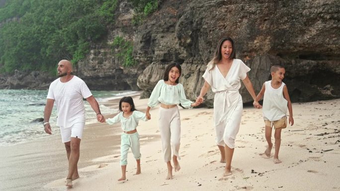 一男一女带着孩子在海滩和海水边散步的快乐家庭。小女孩和男孩的热带旅游与妈妈和爸爸在岸边放松。健康美与