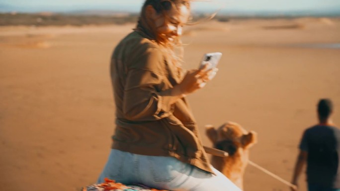 女游客在导游带领下骑骆驼，用手机拍照